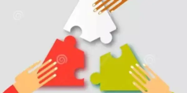 Drei Hände unterschiedlicher Hautfarben legen jeweils ein farbiges Puzzleteil (rot, grün, weiß) in die Mitte auf einem grauen Hintergrund. Die Hände symbolisieren Zusammenarbeit und das Zusammenfügen von Lösungen.