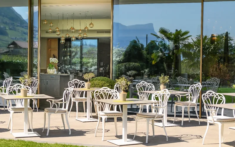 Sonnige Terrasse mit weißen Stühlen und Blick ins Grüne vor dem Restaurant des Hotels